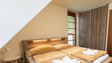 Un dormitorio con cabecera de madera, cama con ropa de cama color beige, lámpara de noche y ventana con persianas.