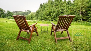 Two wooden Adirondack chairs and a small table set on a grassy lawn with a forest in the background.