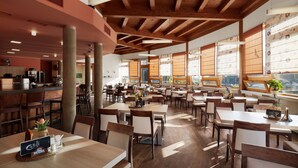 A spacious dining area with wooden tables and chairs, large windows, and a high ceiling with exposed beams. - Wellness hotel Říčky (Rícky v Orlických horách)