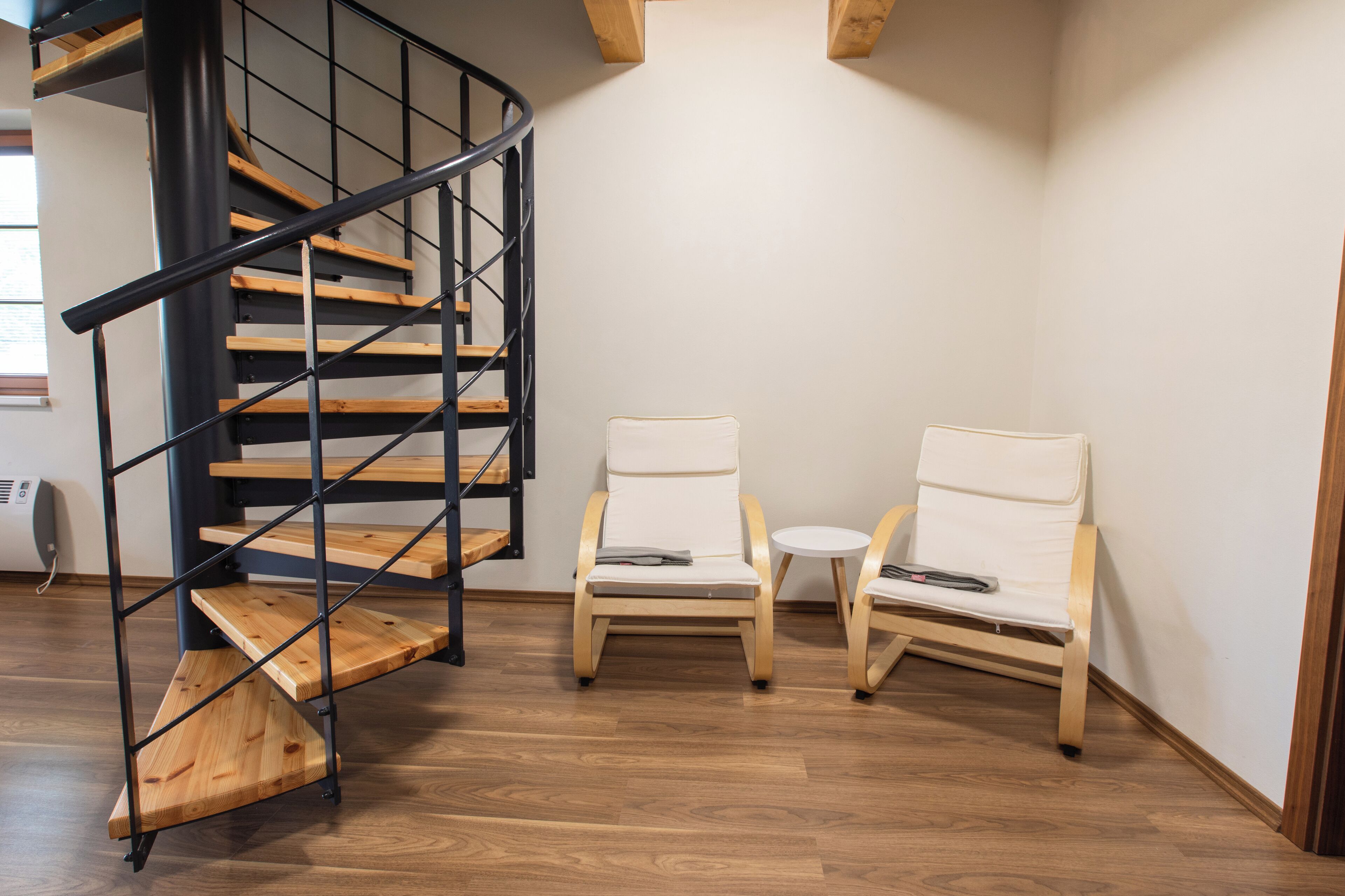 A staircase with wooden steps and black metal railings, two white cushioned chairs, and a small round table.