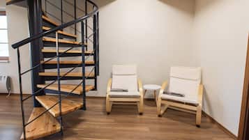 A staircase with wooden steps and black metal railings, two white cushioned chairs, and a small round table.
