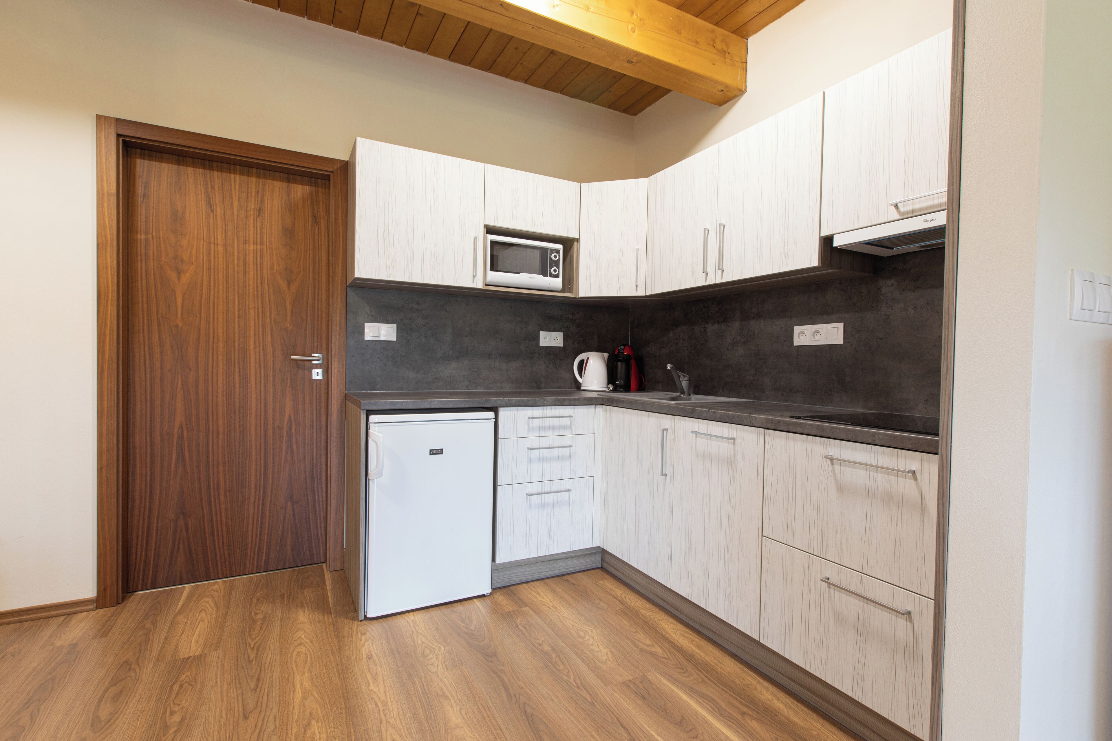 A compact kitchen with white cabinets, a microwave, a coffee maker, and a small refrigerator.