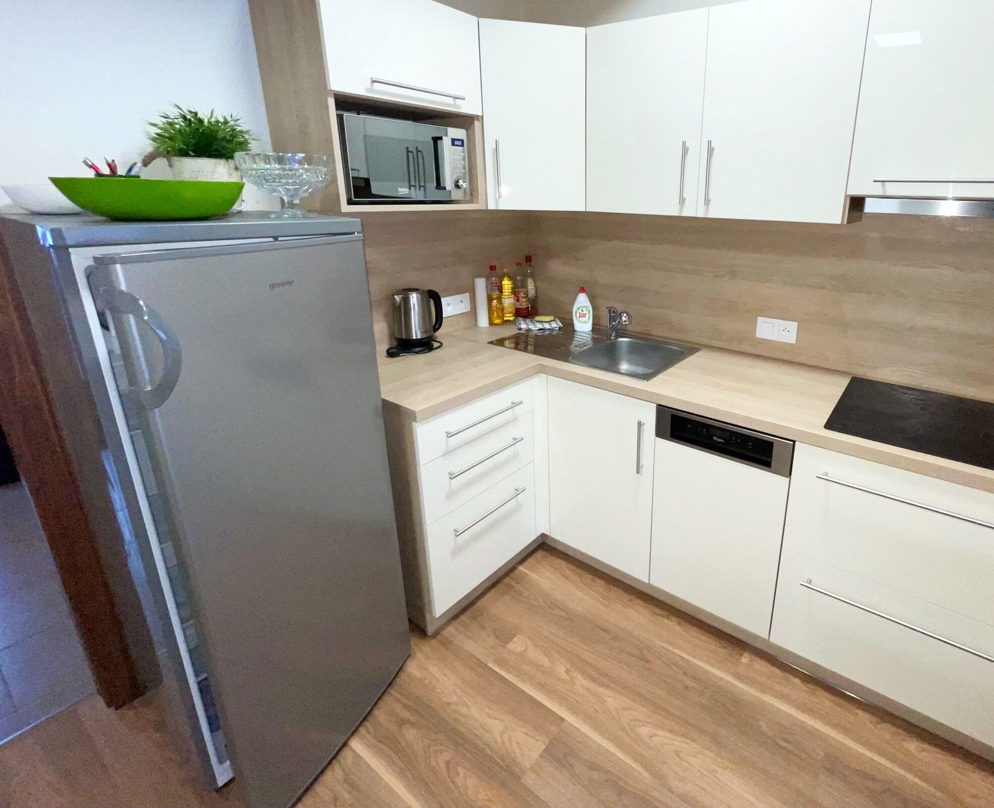 A modern kitchen with white cabinets, a stainless steel refrigerator, a microwave, a sink, and a dishwasher.