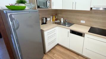 A modern kitchen with white cabinets, a stainless steel refrigerator, a microwave, a sink, and a dishwasher.