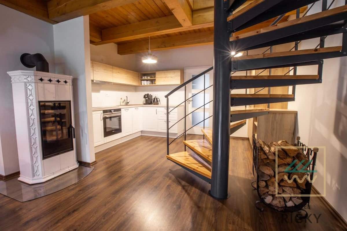 A modern kitchen with white cabinets, a built-in oven, and a wooden staircase.