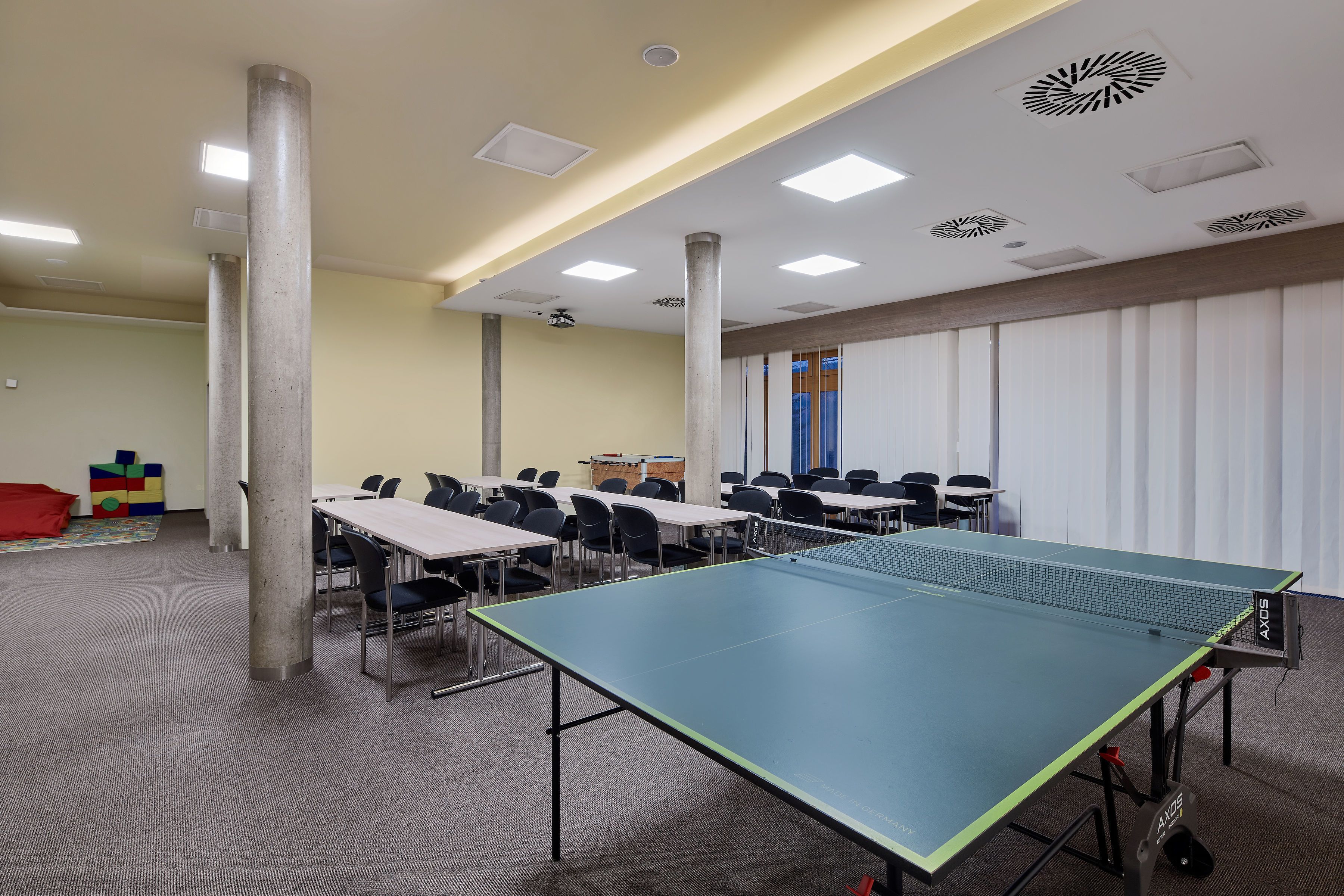 A room with a ping pong table, chairs, and a projector screen.