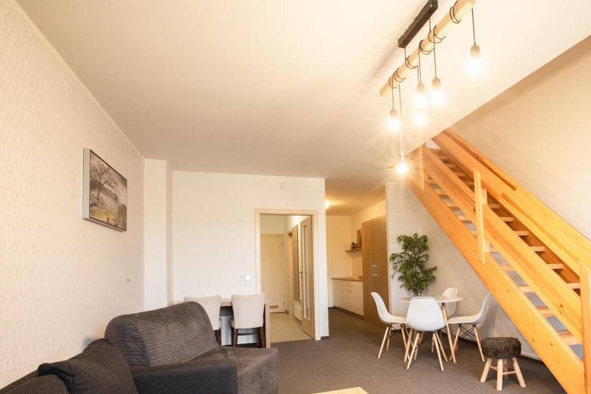 A living room with a sofa, a coffee table, a staircase, and a dining area with chairs and a table.