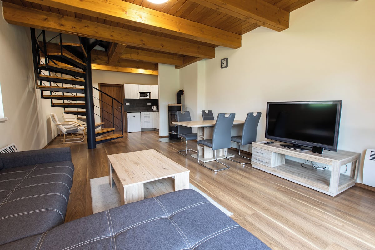A modern living room with a wooden staircase, a dining area, and a kitchen.