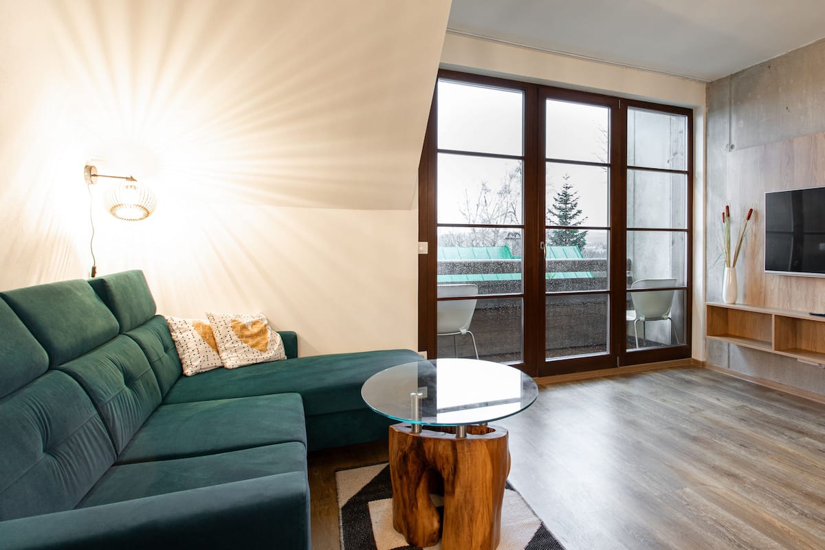 A modern living room with a green sofa, a glass-top coffee table, and a large sliding glass door leading to an outdoor area.