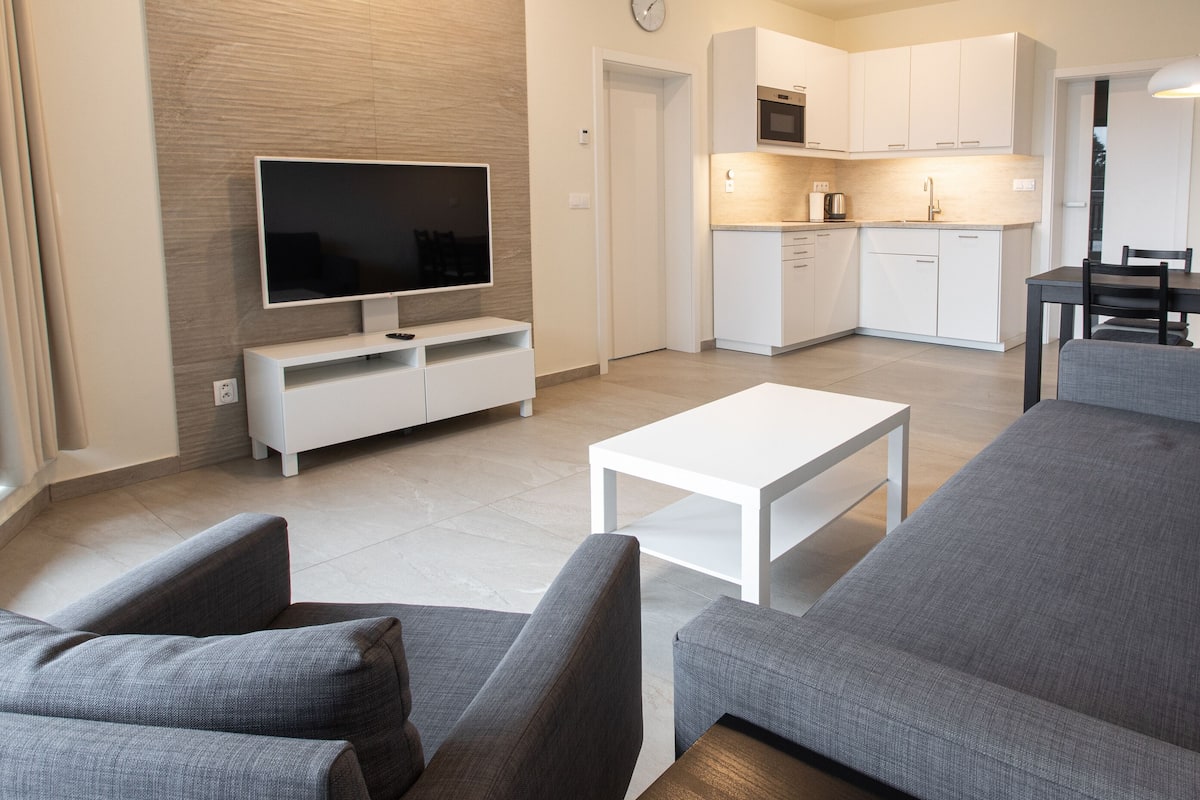 A modern living room with a flat-screen TV, grey sofas, and a white coffee table.