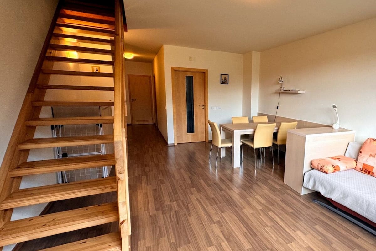 A staircase leading to a second floor, a dining area with a table and chairs, and a sofa with cushions.