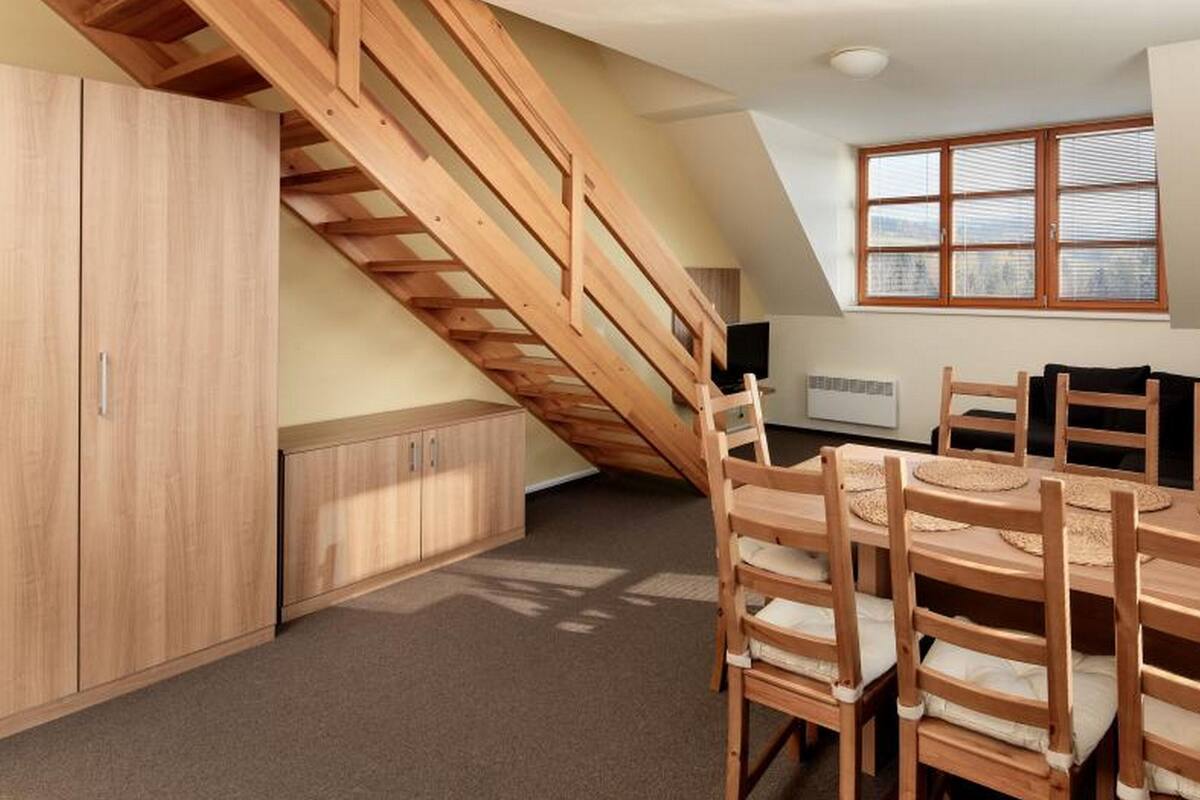 A room with a wooden staircase, a dining table with chairs, and a large window with blinds.