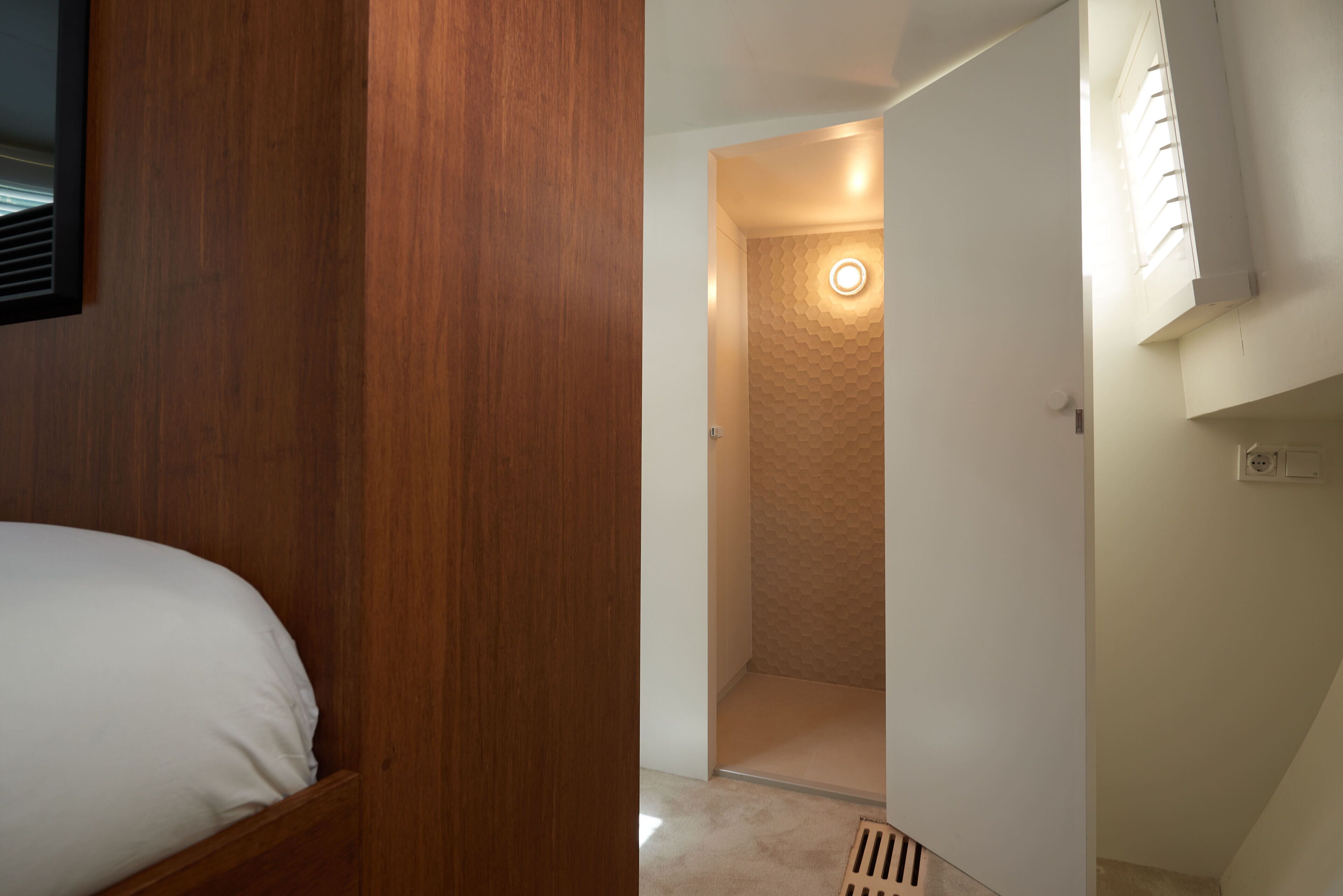 Une chambre avec une armoire en bois, un lit et une salle de bain équipée d’une douche et d’un luminaire rond.