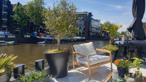 A balcony with a chair, potted plants, and a view of a river with boats.