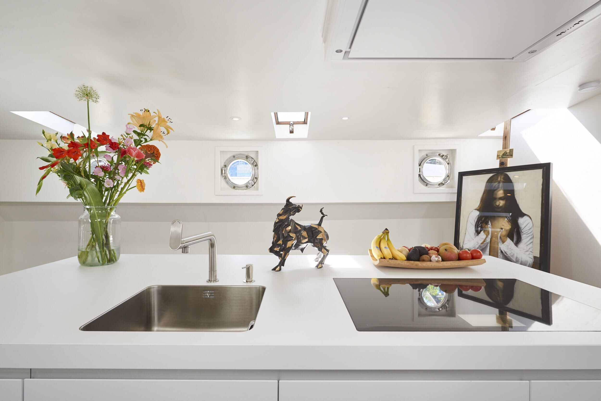 A modern kitchen with a white countertop, stainless steel sink, and a decorative sculpture.