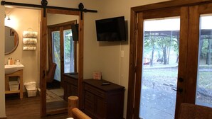 A bedroom with a bed, a wooden bench, a TV, and a sliding glass door to the outside. - Walnut Waters Bed & Breakfast (Lone Jack)
