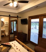 Un dormitorio con cama, un banco de madera, televisor y puerta corrediza de vidrio al exterior.