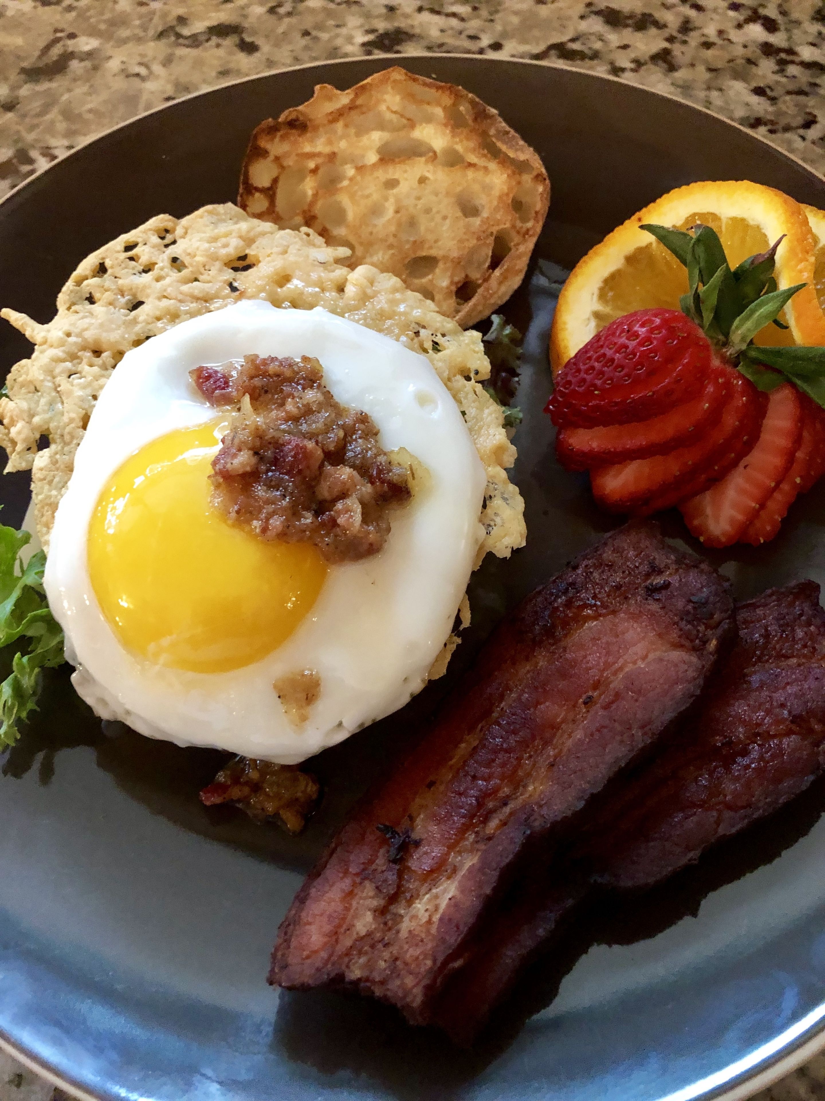 A breakfast plate with scrambled eggs, bacon, toast, strawberries, and orange slices.