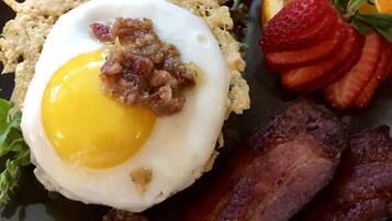 A breakfast plate with scrambled eggs, bacon, toast, strawberries, and orange slices.