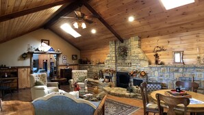A cozy cabin interior with a stone fireplace, wooden walls, and a high ceiling. - Walnut Waters Bed & Breakfast (Lone Jack)