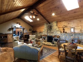 Interior acogedor de una cabaña con chimenea de piedra, paredes de madera y techo alto.
