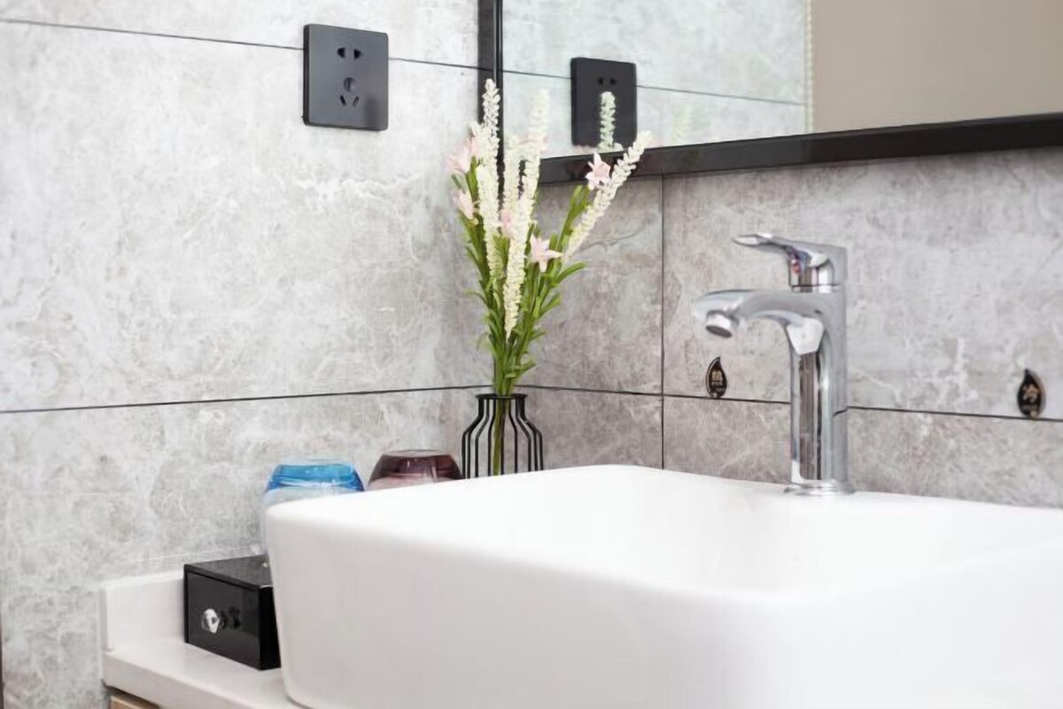 Un bany amb un lavabo blanc, un mirall i un ram de flors.