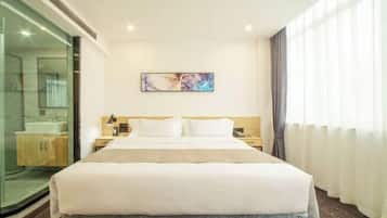 Habitación de hotel con una cama grande, una mesita de noche, una obra de arte en la pared y vistas a un baño con mampara de vidrio.