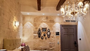 A bedroom with stone walls, a bed with a headboard, a chandelier, and a door.