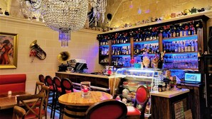 A bar area with a chandelier, a variety of bottles, and a seating area with red chairs and a wooden table.