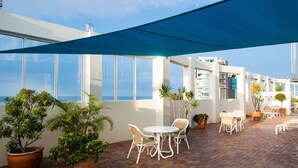 An outdoor patio with white chairs and tables, potted plants, and a view of the ocean. - Beachcomber Beach, Coolangatta (Coolangatta)