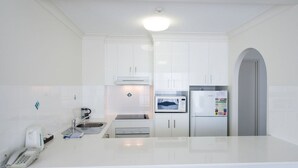 A modern kitchen with white cabinetry, a built-in microwave, a refrigerator, and a coffee maker. - Beachcomber Beach, Coolangatta (Coolangatta)