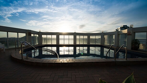 A swimming pool with a curved design, surrounded by a brick deck and large windows offering a view of the sky and distant landscape. - Beachcomber Beach, Coolangatta (Coolangatta)
