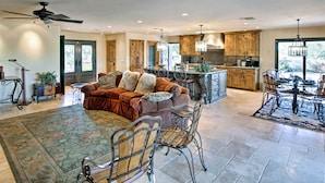 A spacious living area with a sofa, chairs, and a dining table. The kitchen features wooden cabinets and a large island. - Luxe Tucson Vineyard Home w/ Views & Fire Pit (Tucson)