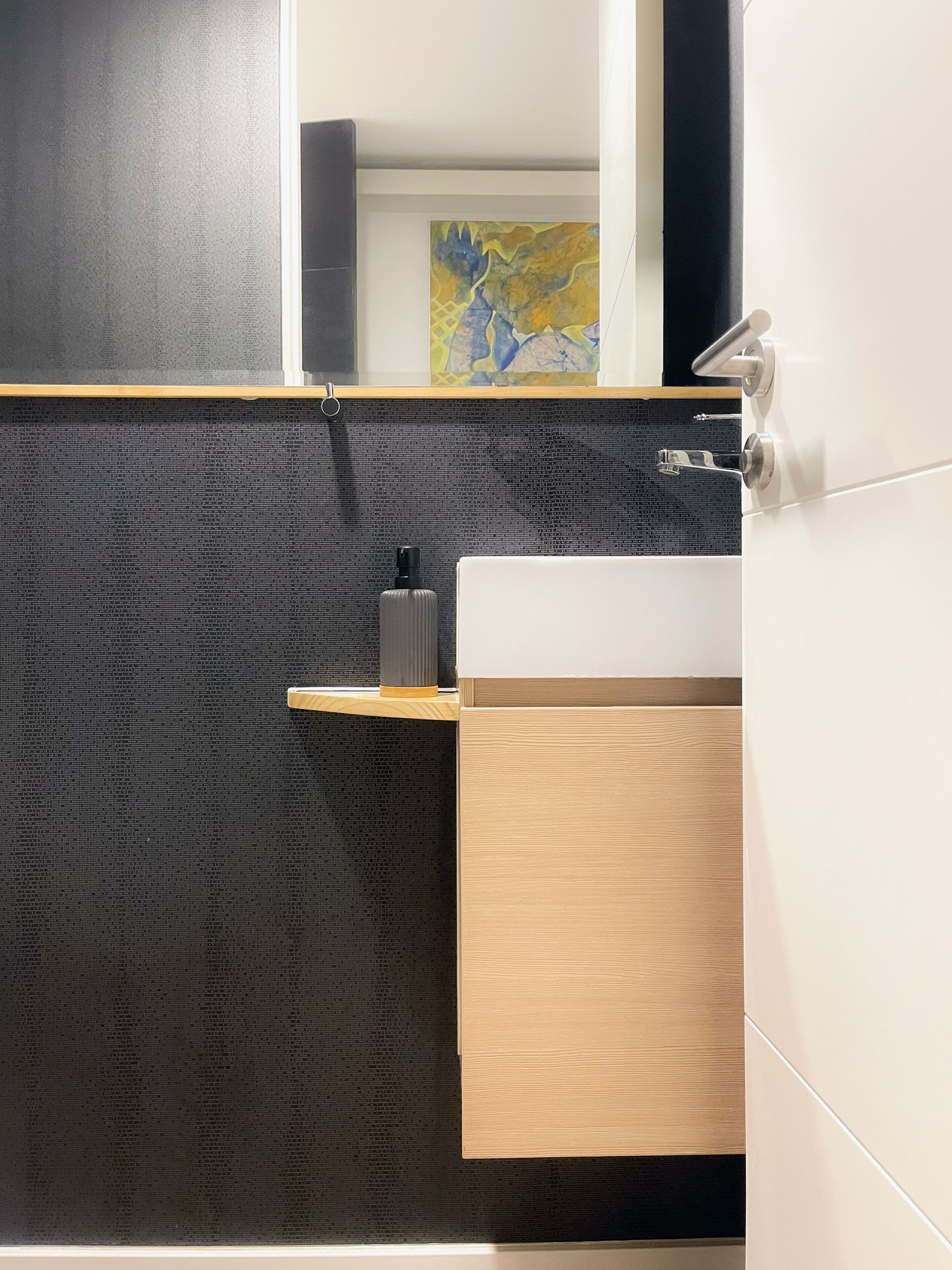 A modern bathroom with a dark textured wall, a wooden vanity, and a white sink.