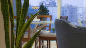 Ein modernes Wohnzimmer mit großem Fenster, einer Topfpflanze und einem grauen Sessel.