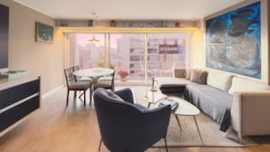 Ein modernes Wohnzimmer mit einer Couch, Sesseln, einem Esstisch und einem großen Fenster mit Blick auf die Stadt.