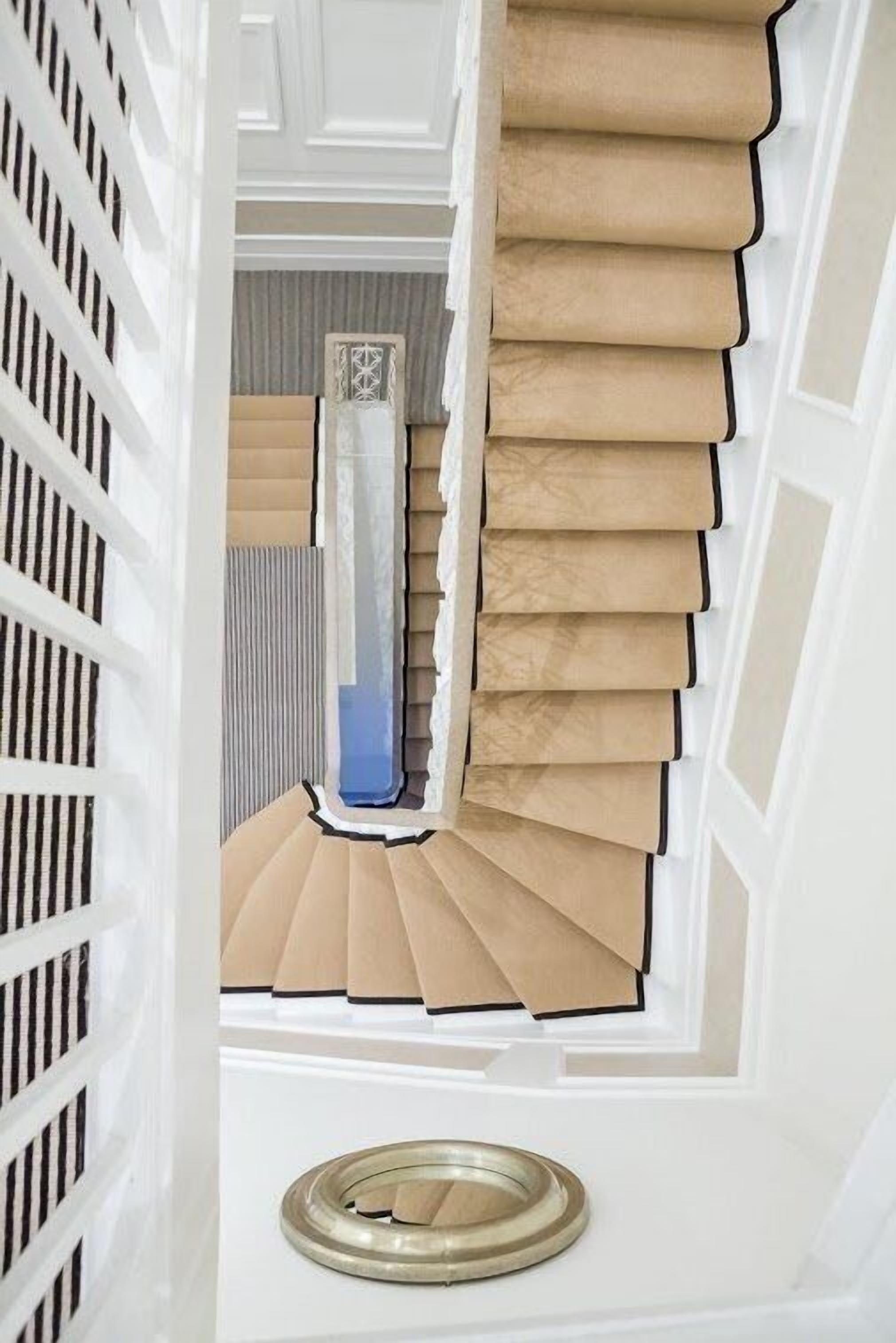 Un escalier aux marches beiges et aux bordures noires, menant à une pièce dotée d’une porte blanche et d’un panneau décoratif mural.