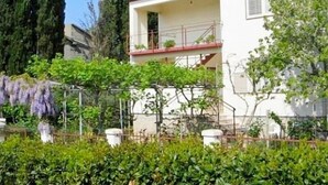 Un bâtiment blanc avec un toit rouge, un balcon et un jardin où poussent différentes espèces de plantes.