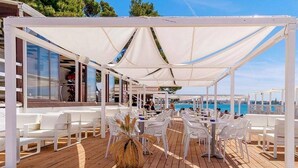 Une terrasse extérieure avec des chaises et des tables blanches, un plancher en bois et une vue sur la mer.