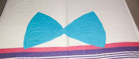 A bed with a blue bow-shaped pillow, a striped blanket, and a pink flower.
