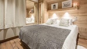 A wooden-paneled bedroom with a bed, white bedding, and a gray textured blanket. - Whistler Lodge Apartment T3 Cabin B07 (Courchevel)
