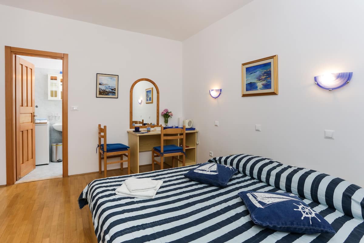 A bedroom with a bed, a desk, and a chair. There is a door leading to a bathroom.