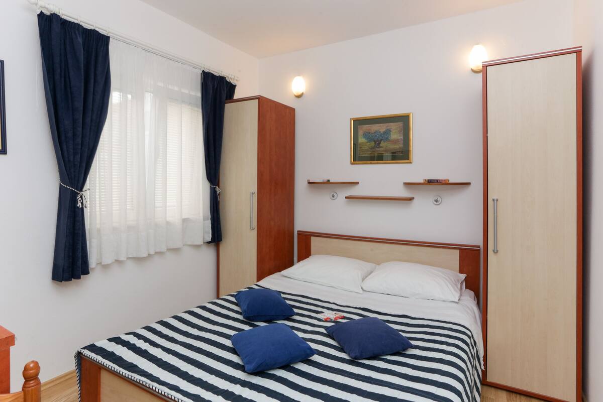 A bedroom with a bed, curtains, a painting, and a wardrobe.