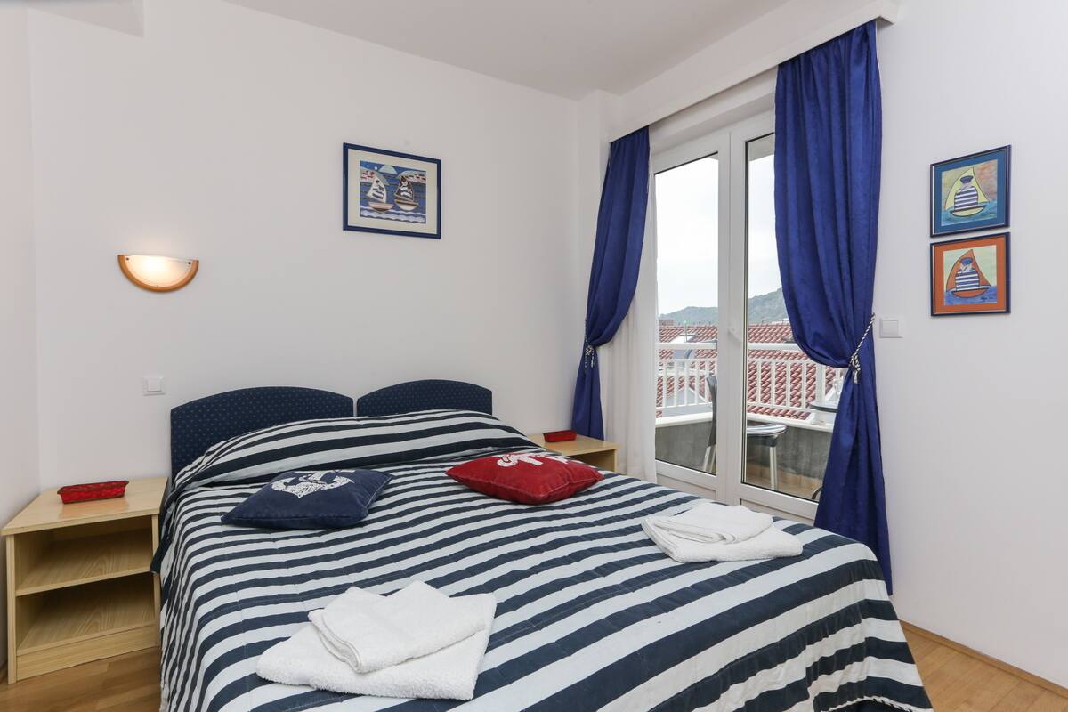 A hotel room with a bed, a nightstand, a window with curtains, and wall art.