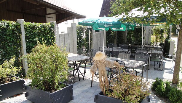 An outdoor patio area with tables and chairs, surrounded by planters and a decorative figure. - Zum Ochsen (Waldstetten)