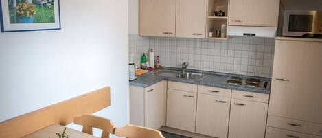 A compact kitchen with a dining area, featuring a sink, stove, cabinets, and a small countertop.