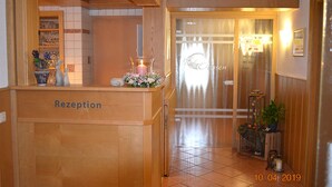 A reception area with a wooden counter labeled "Rezeption," a glass door with a frosted glass panel, and a small potted plant on the right. - Zum Ochsen (Waldstetten)