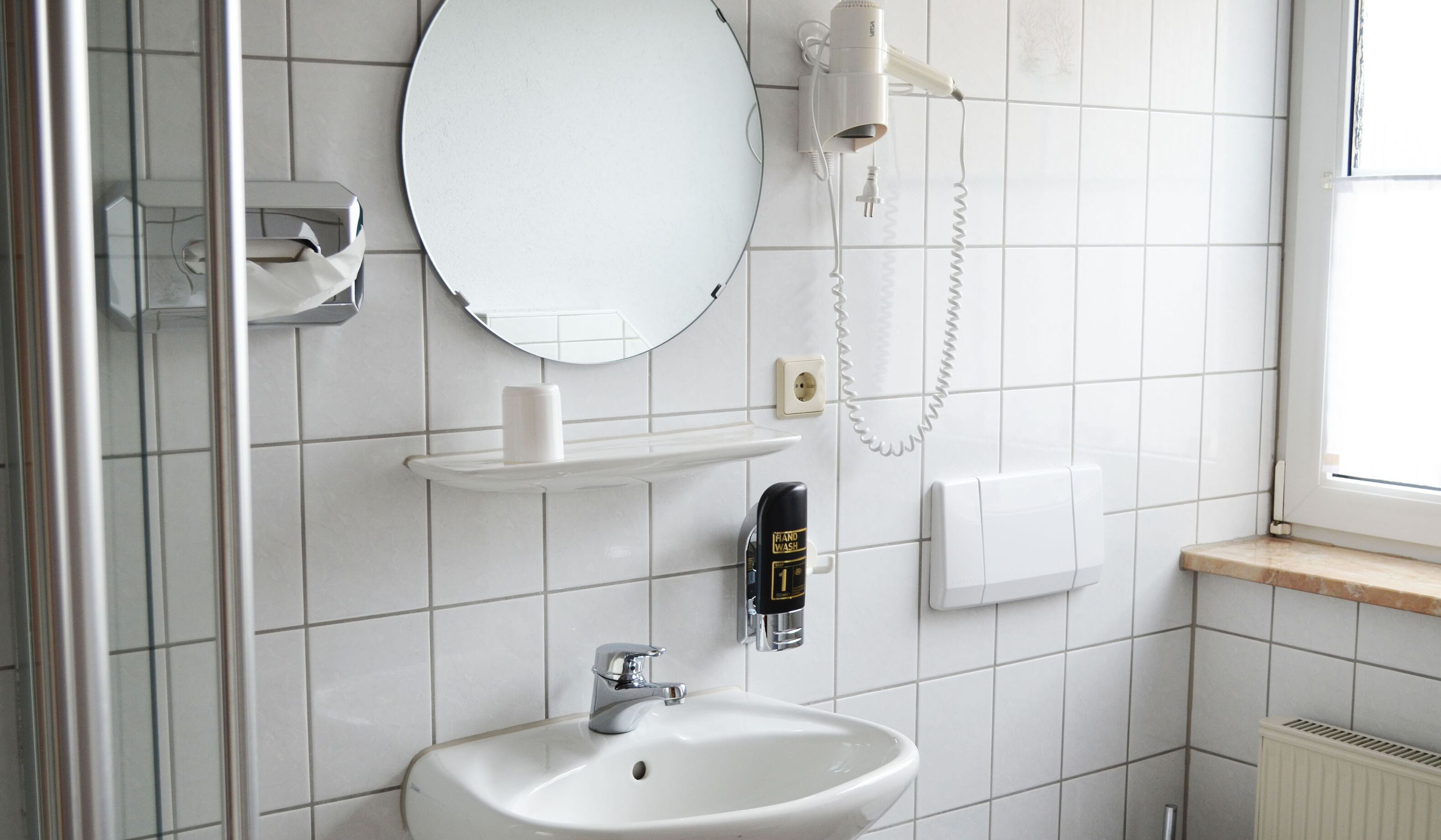 Une salle de bain avec un lavabo blanc, un miroir, un distributeur de serviettes, un sèche-cheveux et un distributeur de savon.