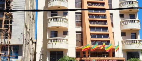 Un hotel de varios pisos con balcones, una entrada principal y banderas.