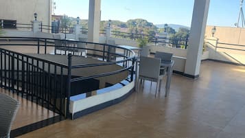 A spacious outdoor terrace with a curved railing, tiled flooring, and a view of distant hills.